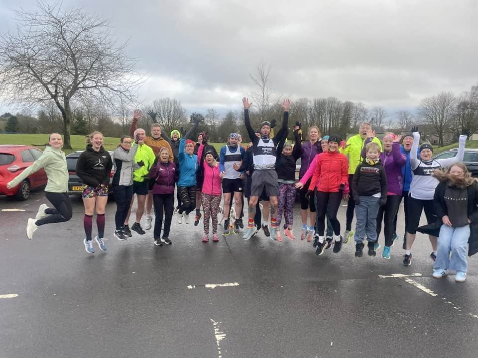 Group of junior and adult runners in running kit jumping in the air
