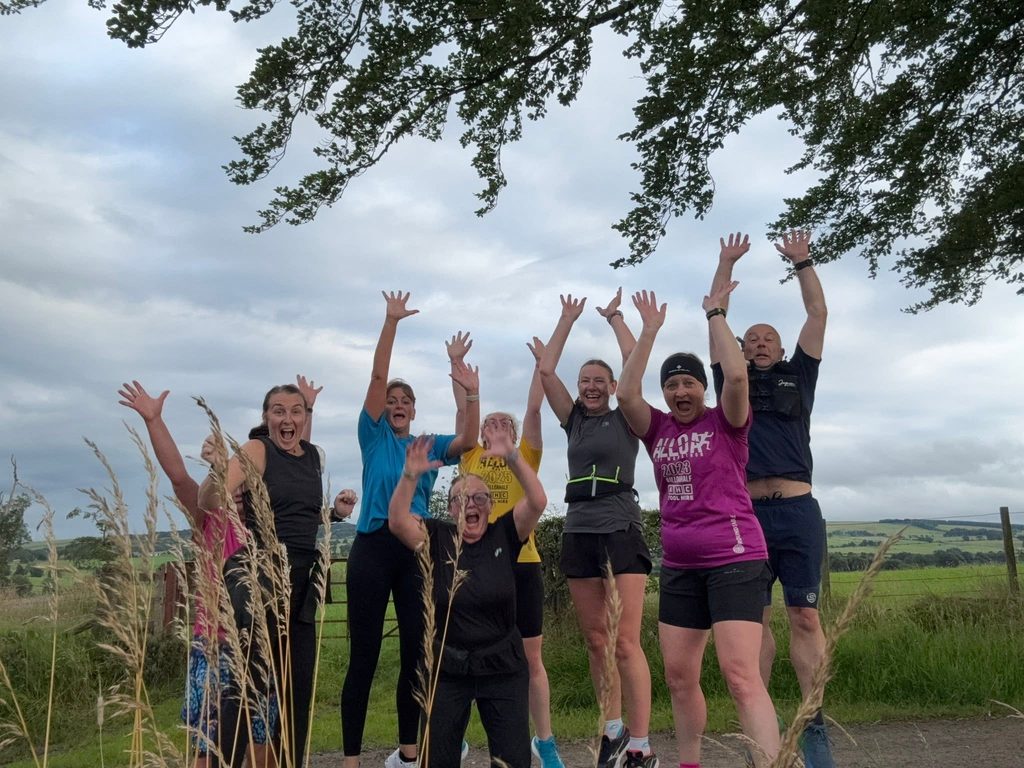 Group of runners jumping in the air with their arms above their heads.