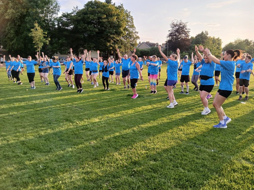 Group of people in blue t-shirts in a park doing a warm up before their run
